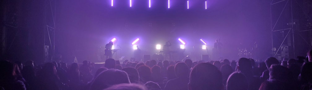 Salle de concert vue de dos, lumières violettes sur scène